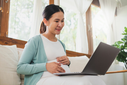 Asian pregnant woman using laptop computer at home