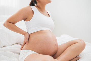 Fototapeta na wymiar Asian young pregnant woman with big belly has backache, back pain on bed