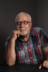 Fototapeta premium Elderly charismatic man in a checkered shirt, wearing glasses looks to the side with interest, close-up portrait on a gray background