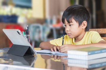 Portrait image of 7-8 years old kid. Happy Asian student child boy using and touching smart pad or tablet for do his homework and online learning (E-learning). Back to school, Study from home.