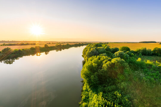 Scenic view at beautiful summer river sunset with reflection on water with green bushes, grass, golden sun rays, calm water ,deep cloudy sky and glow on a background, spring , evening landscape © Yaroslav