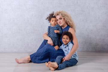 Caucasian young mother with curls hugs African American children. Happy mixed race family adoption