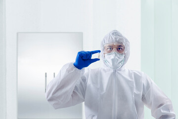Fototapeta premium Health worker man with a protective suit and gloves holding covid 19 vaccines