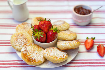 Syrniki or cottage cheese fritters with strawberry jam on a white plate. 