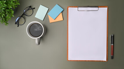 Empty clipboard, coffee cup and colorful sticky notes on green background.