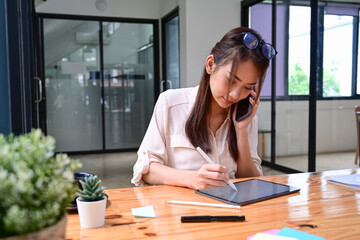 Woman entrepreneur talking on mobile phone and working with digital tablet.