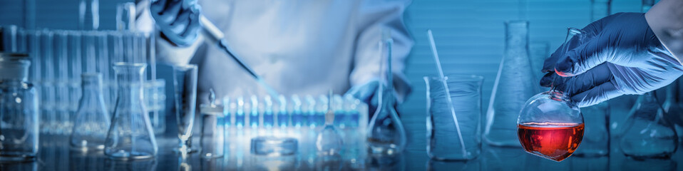 Scientist holding flask with lab glassware in chemical laboratory background