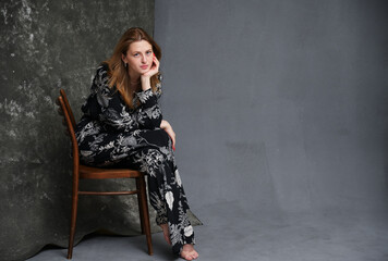 High resolution portrait of european model sitting on chair against dark background in studio