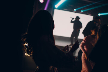 Singer man silhouette in the dark sings into a microphone at a concert.