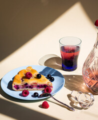a piece of berry pie with curd or cheese filling and raspberries and blackcurrant compote in crystal bottle under hard light, art composition with harsh shadows