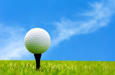 Golf ball on tee ready to shot on green grass over blue sky 