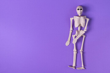 Halloween background with human skeleton on purple background top view. Halloween greeting card.