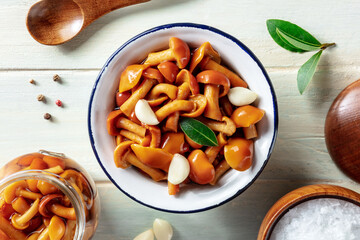 Pickled mushrooms with garlic, salt, pepper, and a bay leaf, shot from above on a rustic wooden background