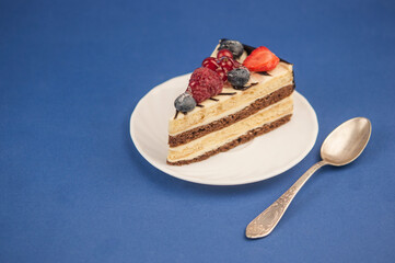 Mix berry slice cake on plate with vintage spoon on blue paper background