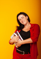 Naklejka premium woman on a yellow background with books in her hands, posing on an isolated background. Business woman in red suit in a dreamy, joyful mood