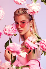 Portrait of beautiful blonde woman in pink ribbed jumpsuit and sunglasses with pink peony around