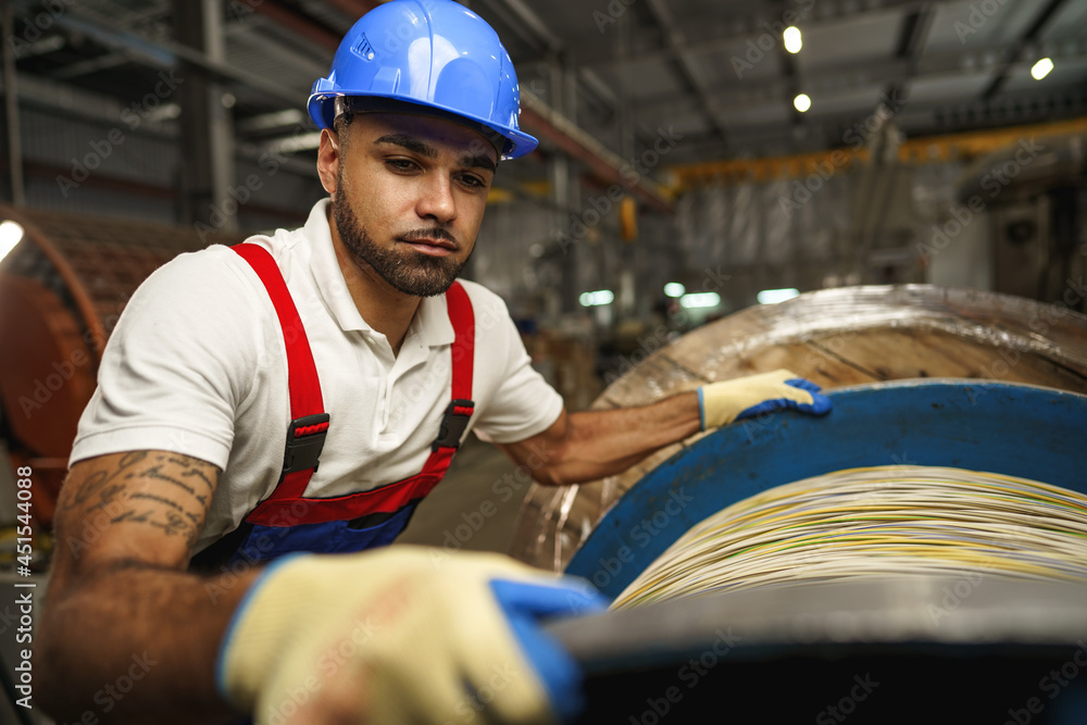 Wall mural A young factory workman rolls heavy coil of electric cable