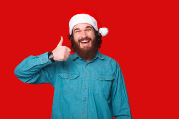 Young handsome man wearing santa claus hat over red background doing happy thumbs up gesture