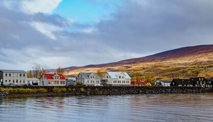 Rows of unique Icelandic building lining up between the mountain range and the lake on a autumn afternoon. Akureyri, Iceland