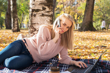 Young woman working with laptop outdoors and talking on the phone