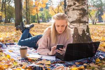 Young woman working with laptop outdoors and holding phone