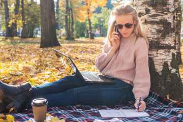 Young woman working with laptop outdoors and holding phone