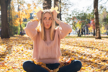 Young pretty woman is sitting on tground in autumn park with leaves in her hands