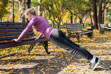 Young woman does push-up exercises in the park. Sports outside in autumn