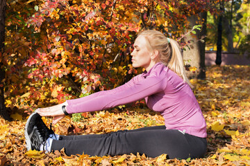 Young woman does stretching exercises in the park. Sports outside in autumn