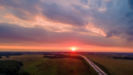 Aerial view of highway on red sunset. Landscape with road near countryside fields. Beautiful winding road leading through rural countryside with evening sunlight. Dramatic sky background.