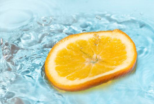 falling orange skin splashing water on a blue background © Thiradech