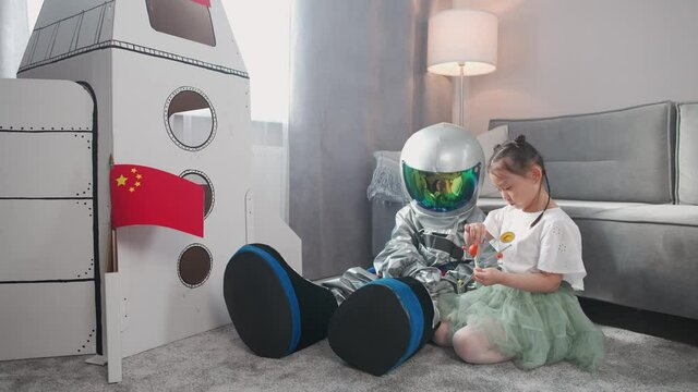 Asian kids play in the living room at home, a boy in an astronaut costume sitting on the floor with her sister, kids playing with a toy model of the solar system, 4k slow motion.