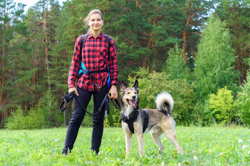 A young girl in a red shirt with her dog stands against the background of the forest. Walking with a pet