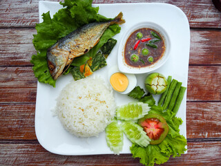 Cooked Jasmine Rice, shrimp paste chili paste, mackerel, boiled egg and fresh vegetables in white plate on brown wooden table. Quick One dish set menu. Thai Food background.