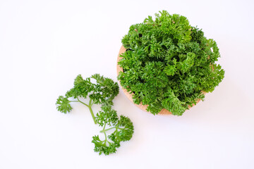 Flat lay composition with fresh green curley parsley leaves in the wooden bowl isolated on white background. One variety of Europe’s most popular herbs. 
