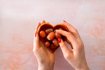 Women's hands holding a plate in the shape of a heart and selecting a grape. Spanish tradition of eating 12 grapes at midnight on New Year’s Eve. It symbolizes 12 lucky months ahead. - obrazy, fototapety, plakaty