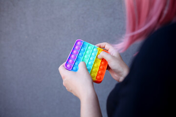 Girl with rainbow Pop It Fidget in hands. Teen Playing, Push bubble on Pop it Fidget.