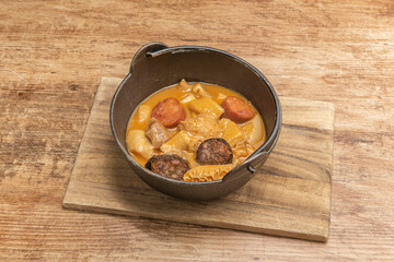 Hanging metal pot with Madrid-style tripe stew with chorizo and rice blood sausage on wooden table