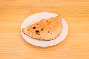 Typical Italian calzone stuffed with four cheeses on a white plate