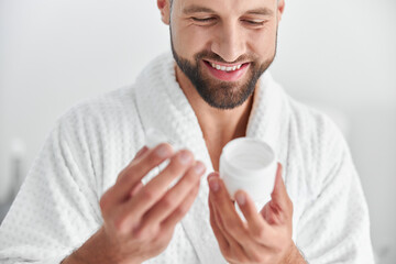 Happy mature man looks at open jar of cream in professional cosmetologycal clinic