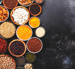 Set of superfoods, legumes, cereals, nuts, seeds in bowls on black table. Copy space, top view