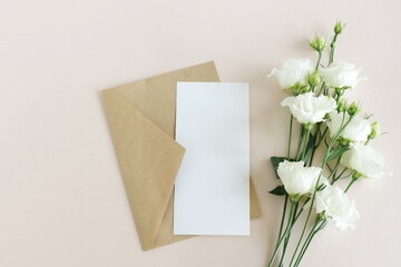 Blank greeting card, envelope and white flowers bouquet top view on beige background .Copy space. Flat lay. Greeting card mockup, sheet paper card for text. Holiday backdrop.