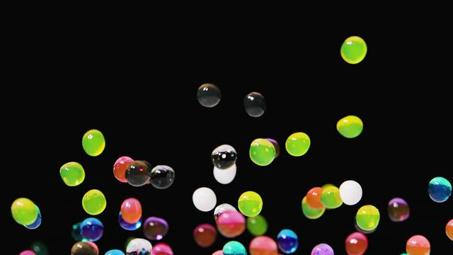 Bright multicolored water gel balls bouncing against a black background. Polymer gel. Silica gel. Hydrogel balls bouncing and fly in different directions caused by sound vibrations. Close up. Slow