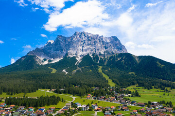 Panoramic drone view from Grubigstein, with rugged Zugspitze in background under blue sunny sky with cumulus clouds. Green valley at the foot of majestic alpine mountains, in Lermoos, Tyrol,