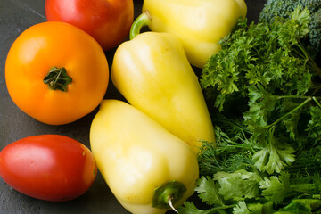 Vegetables: tomatoes, parsley, cilantro and peppers on a dark background.