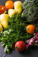 Green vegetables, broccoli, peppers, cabbage, tomatoes and garlic on a dark background, top view.