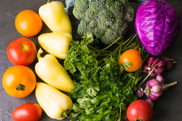 Green vegetables, broccoli, peppers, cabbage, tomatoes and garlic on a dark background, top view.