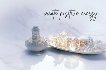 Create positive energy - motivation quote. Clear quartz minerals and Buddha statue on marble background. Magic gemstones crystals for healing esoteric spiritual practice, relaxation and meditation