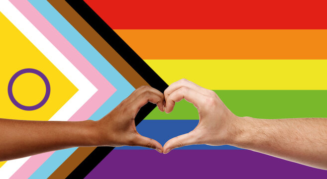 lgbtq, trans and intersex rights concept - close up of couple wearing rainbow ribbon wristbands and showing hand heart over progress pride flag on background