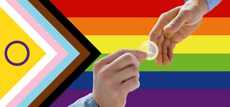 homosexuality, safe sex, sexual education and charity concept - close up of male gay couple hands giving condom over rainbow progress pride flag on background